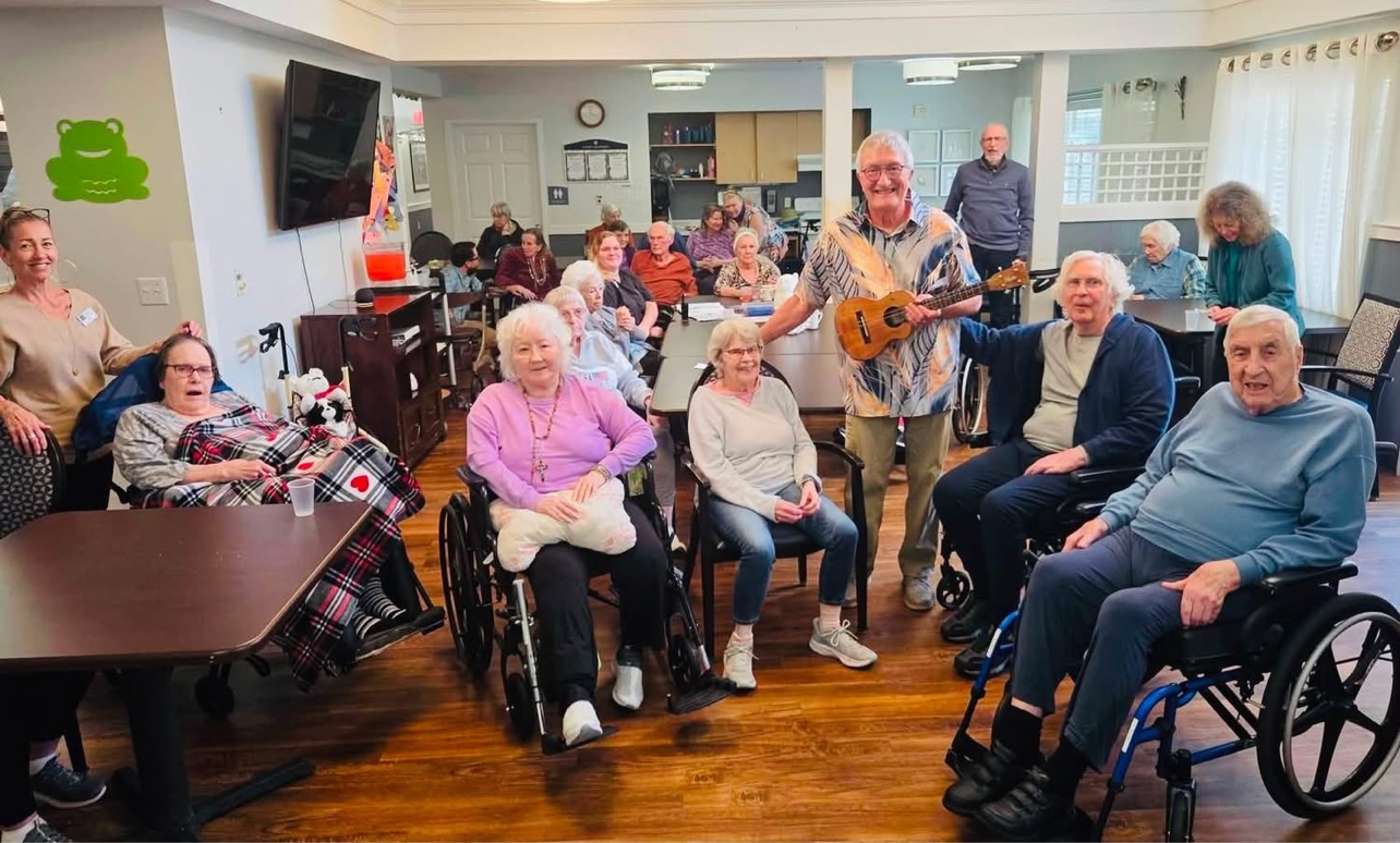 Jerry holding his ukulele, surrounded by smiling residents after a memory care sing-along